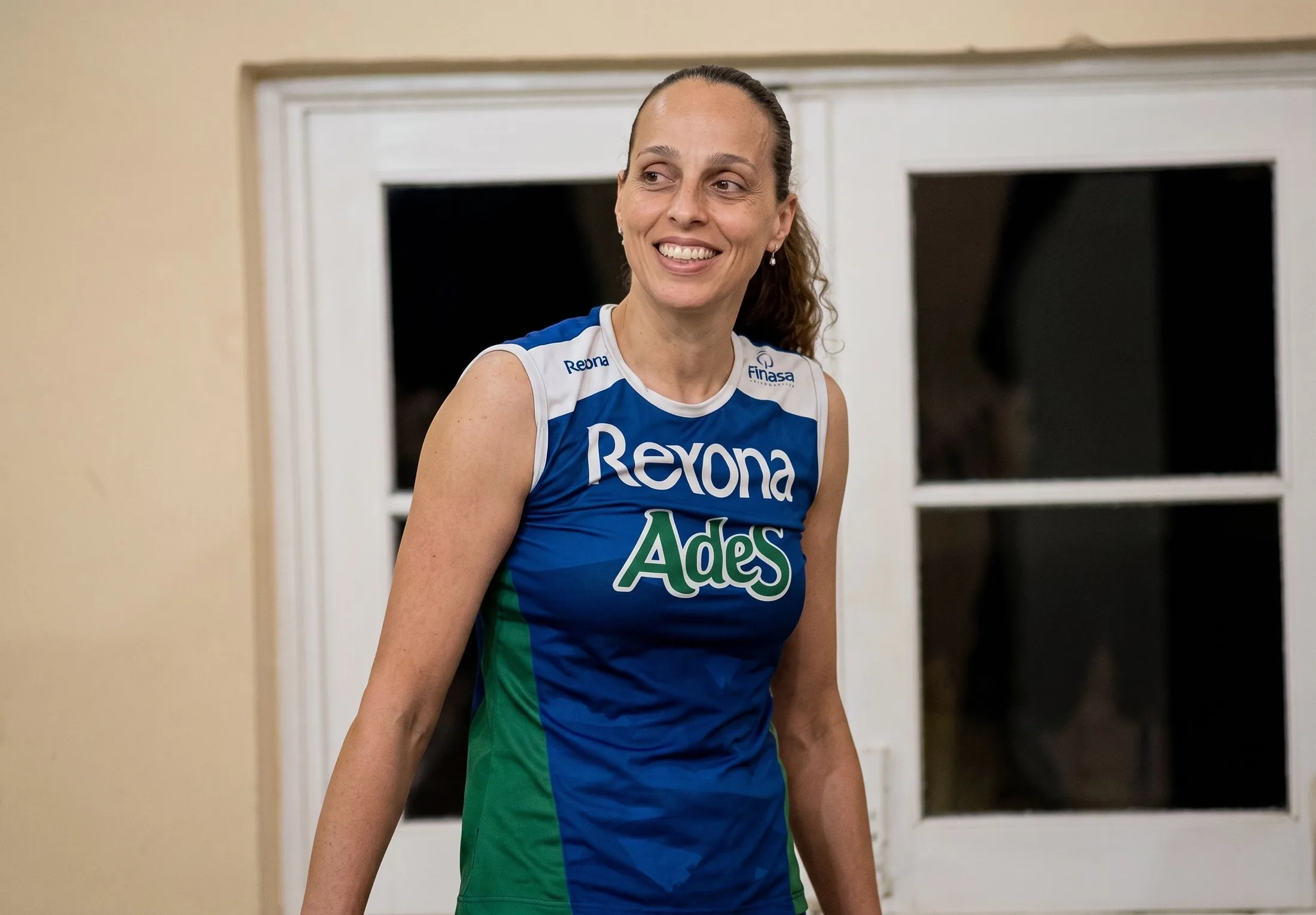 Paula do Vôlei sorrindo em uniforme de atleta durante sua trajetória no esporte.