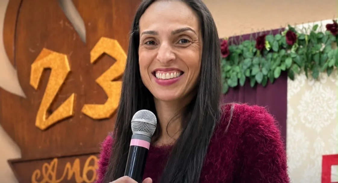 Paula do Vôlei falando ao microfone durante um evento.