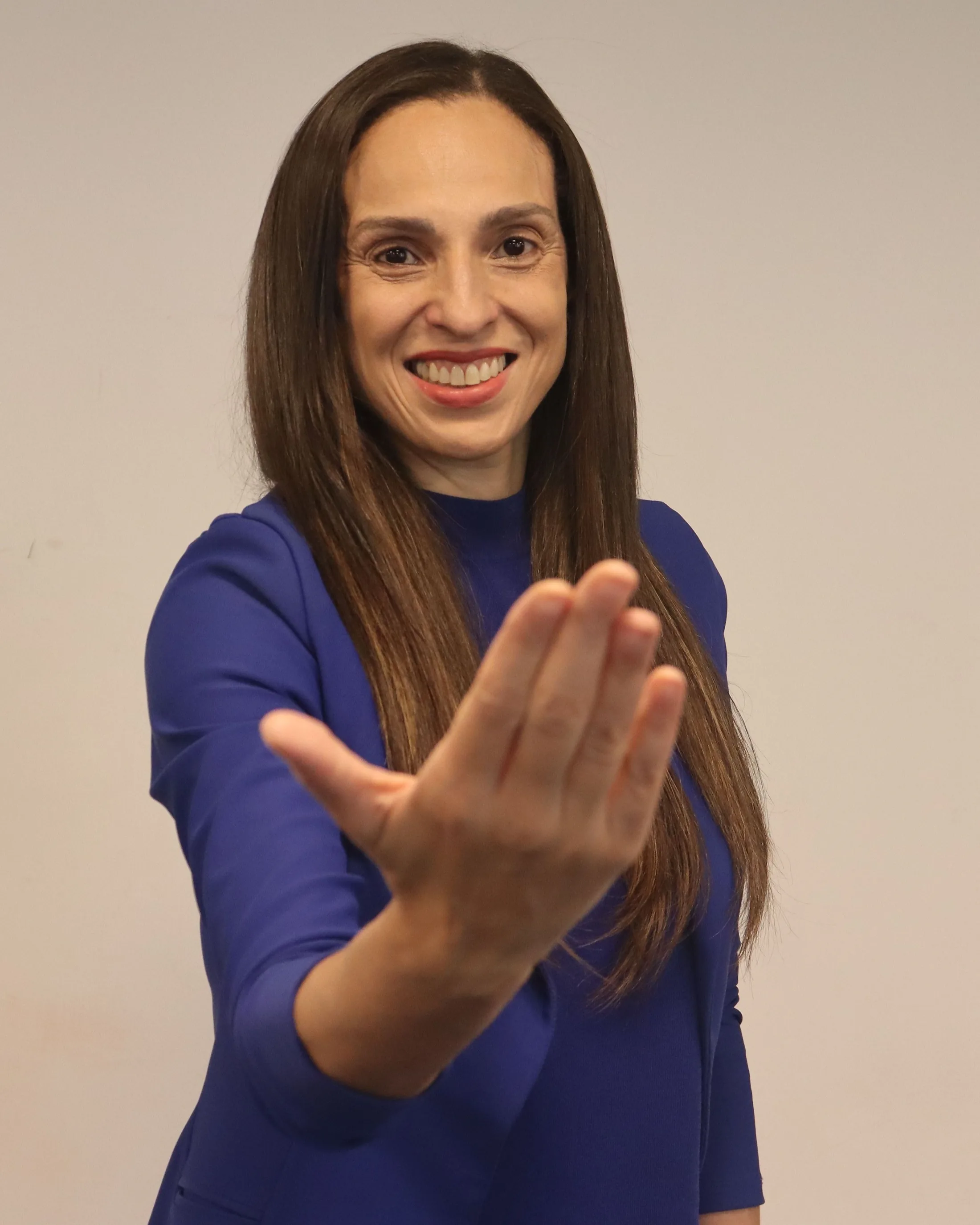 Paula do Vôlei sorrindo com a mão estendida em gesto de acolhimento.